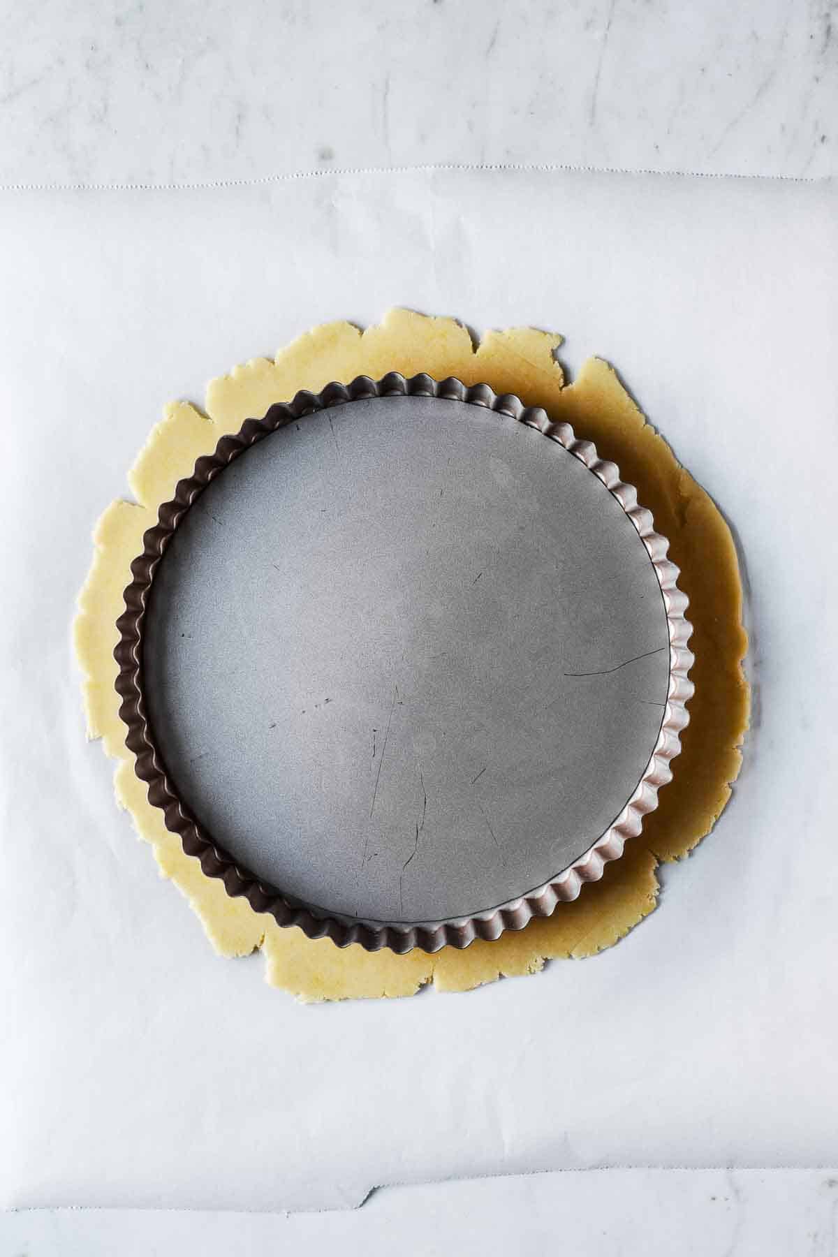 A tart pan resting on top of rolled out sweet tart dough to check the size.