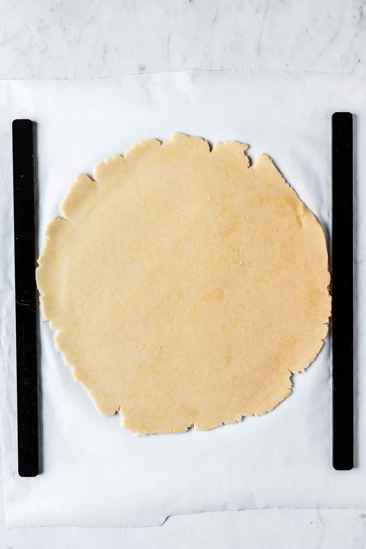 Sweet tart dough rolled out on parchment between black thickness guides.