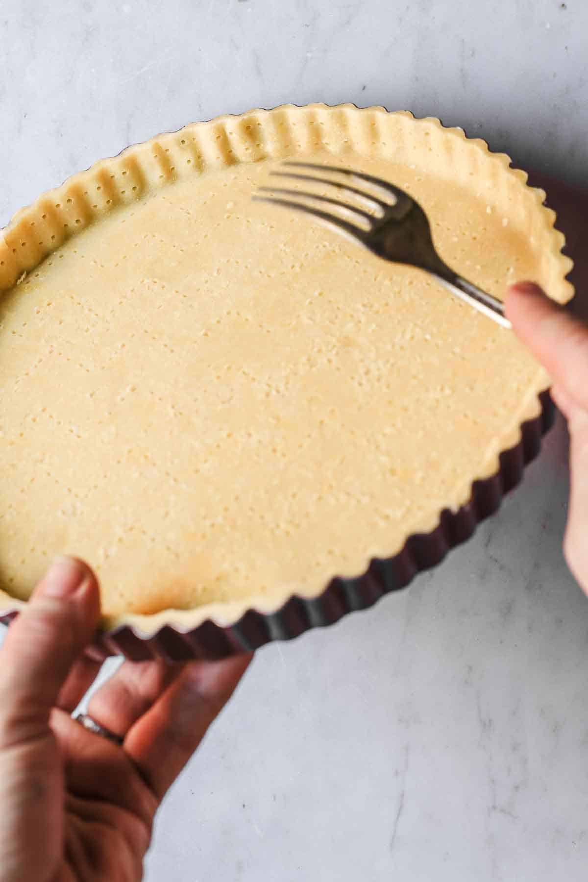 Hands holding a fork to dock sides of tart crust.