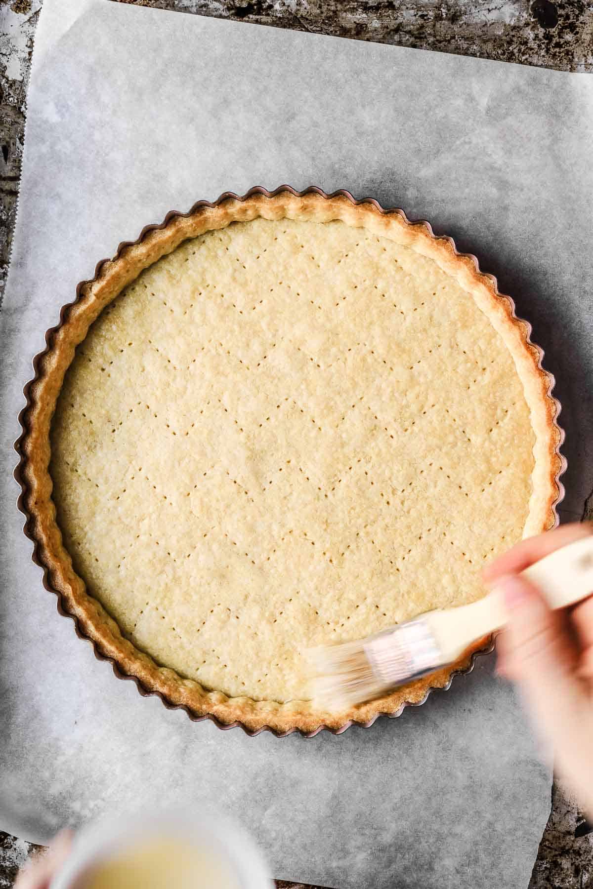 Parbaked tart crust that is being brushed with egg wash.