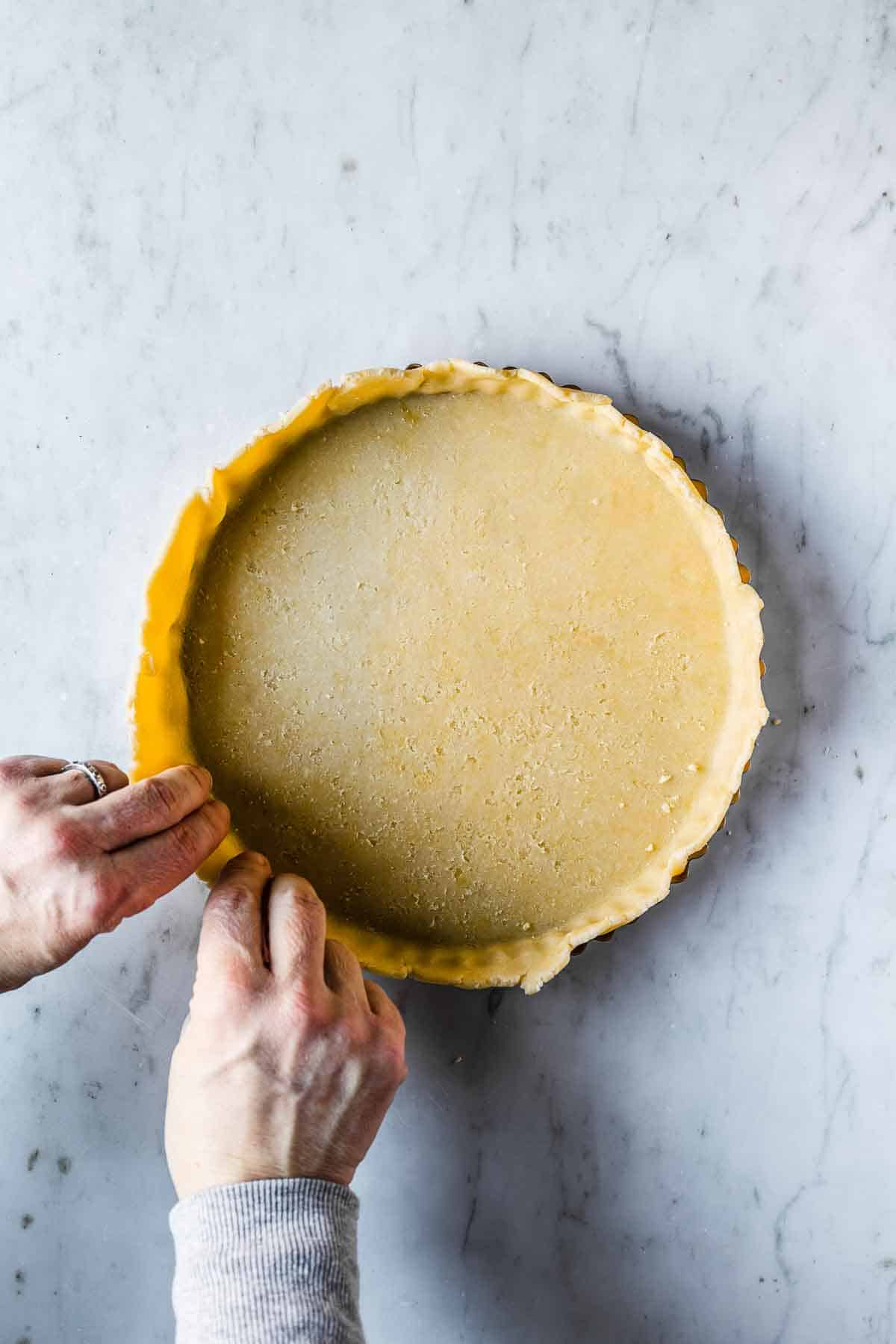 Tart dough being pressed into a fluted tart pan.