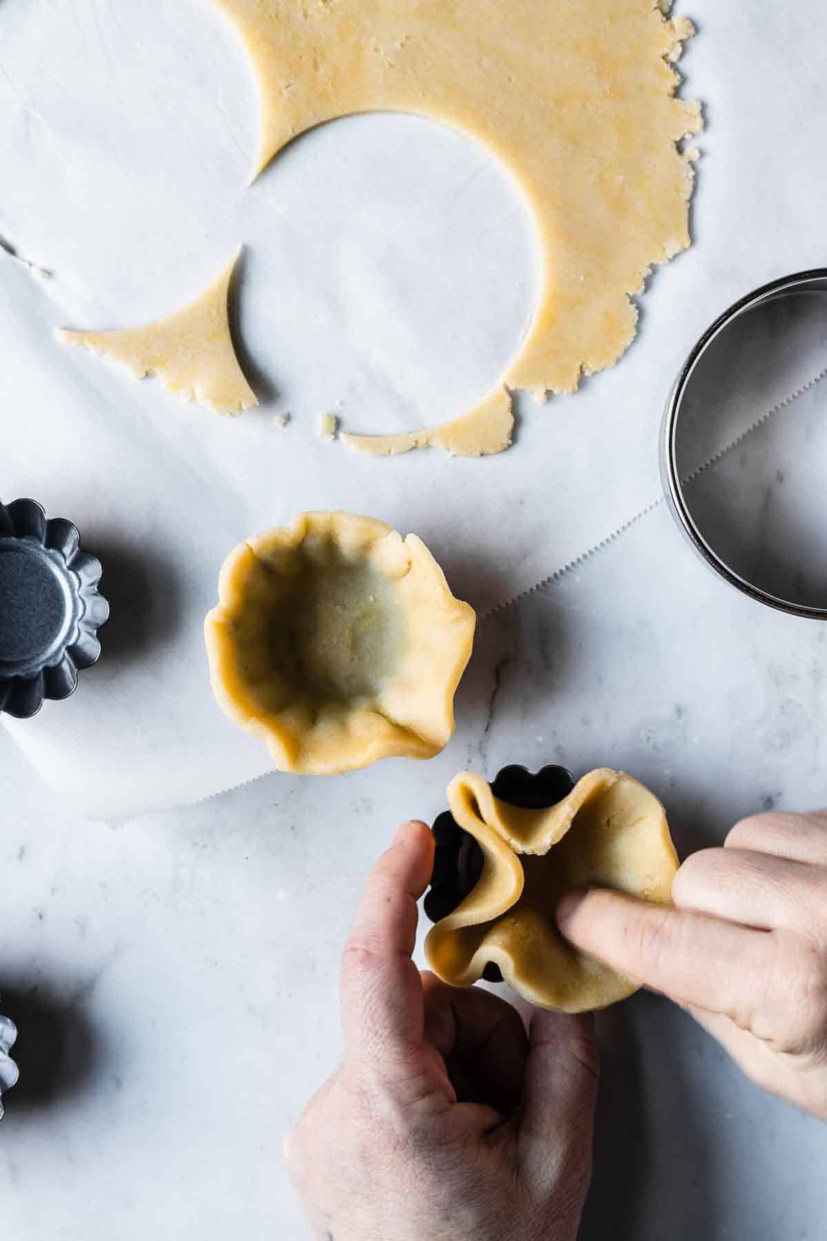 Dough being pressed into small tartlet pans.