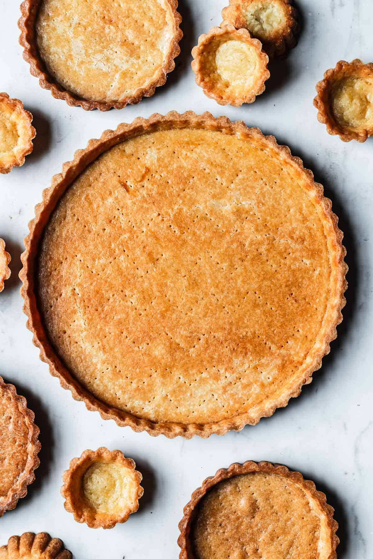 A golden brown baked pate sucree surrounded by mini tart crusts and even smaller tartlet crusts.