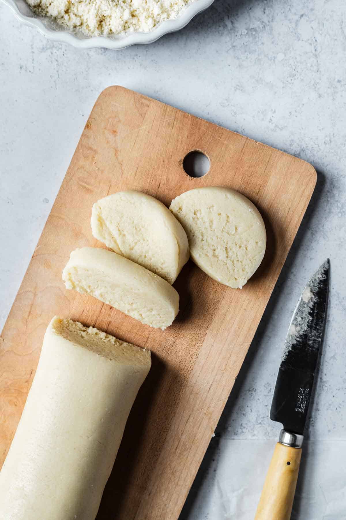 A log of almond paste sliced into rounds on a cutting board.