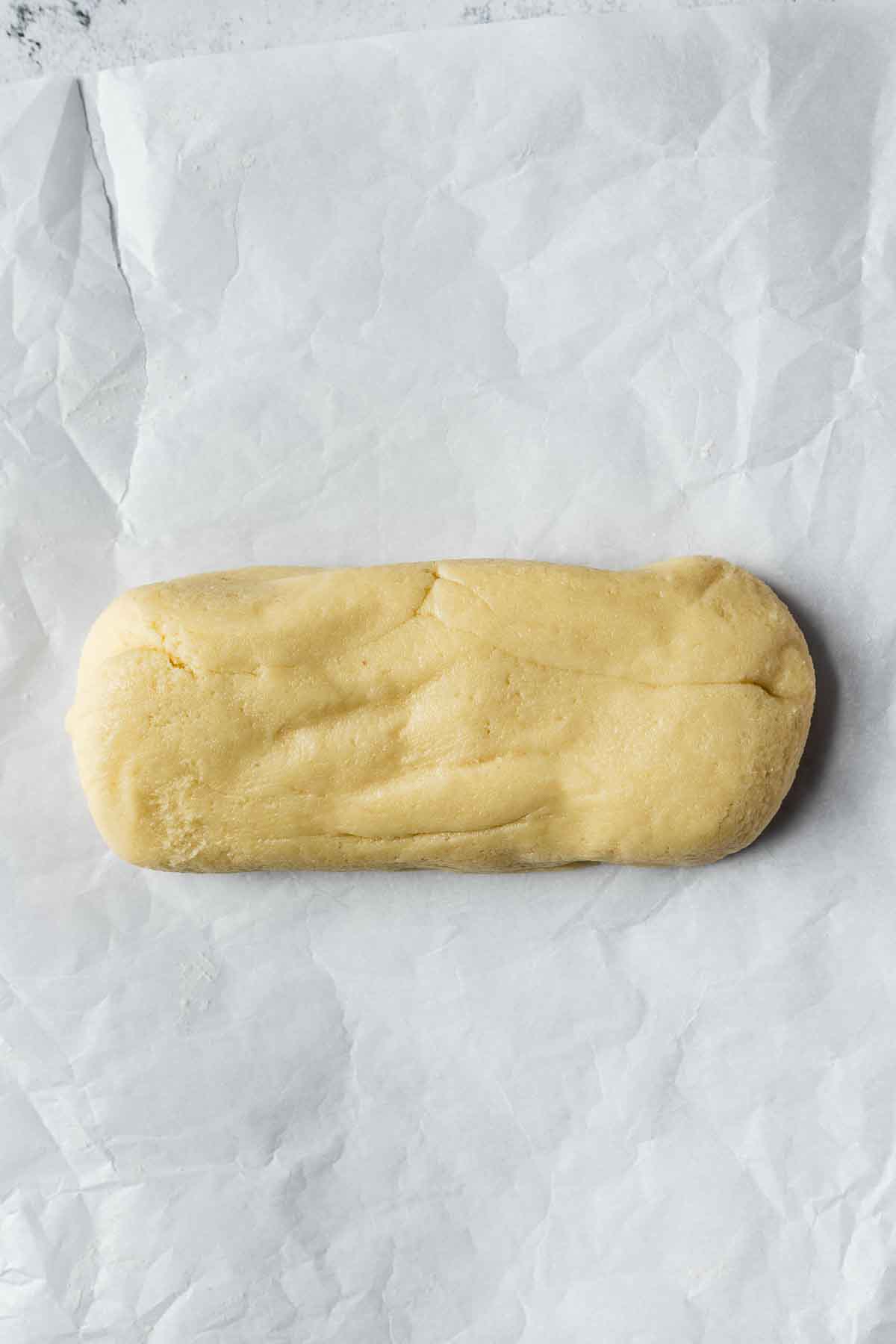 A log of almond paste on white parchment paper.
