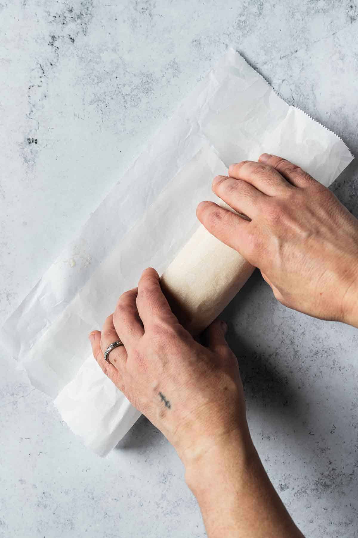 Hands rolling a log of almond paste into parchment paper.