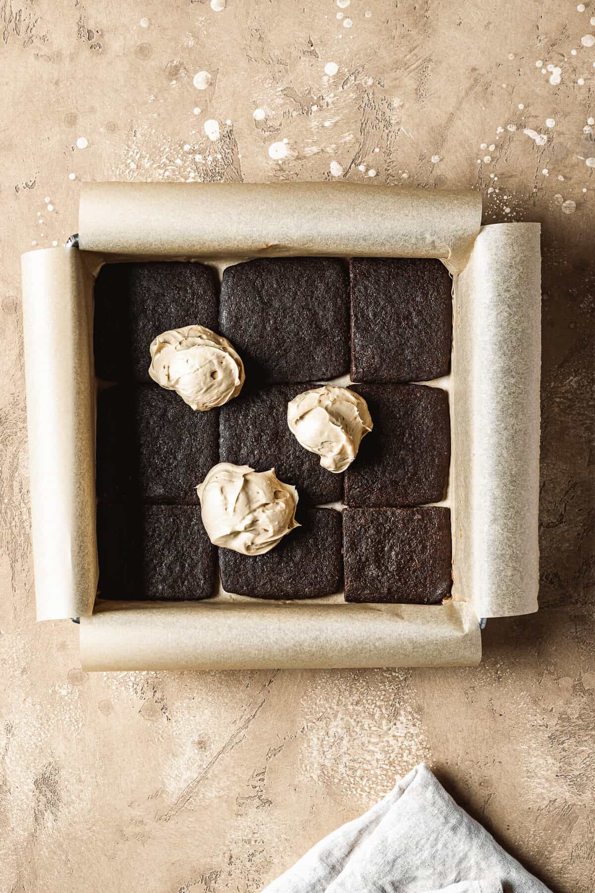 Scoops of dulce de leche filling on a layer of chocolate wafer cookies in a square pan.