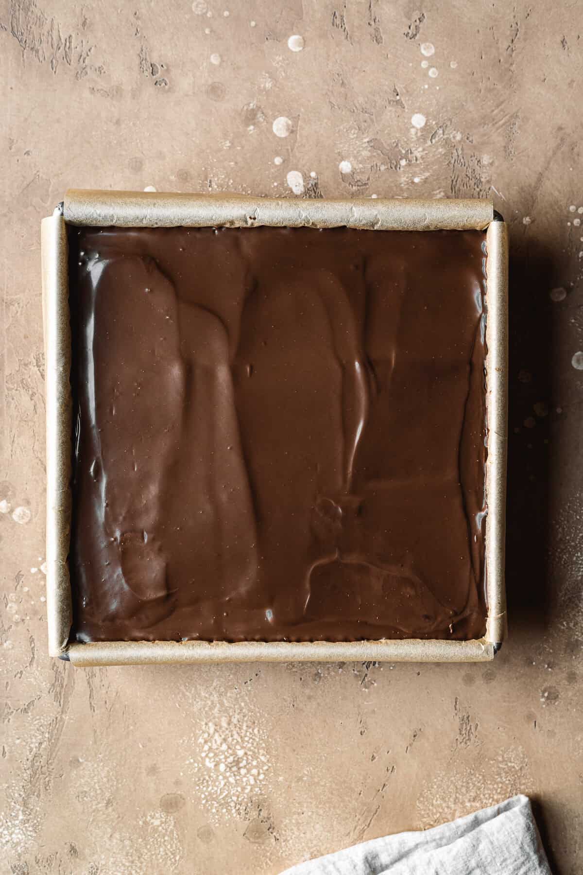 A top layer of dark chocolate ganache in a square pan.