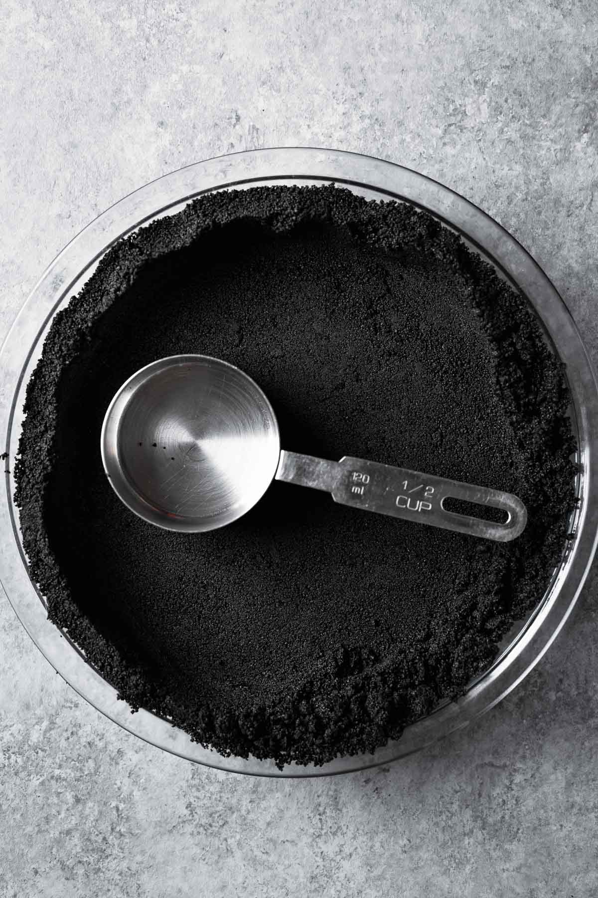Cookie crumbs being pressed into a pan with a measuring cup.