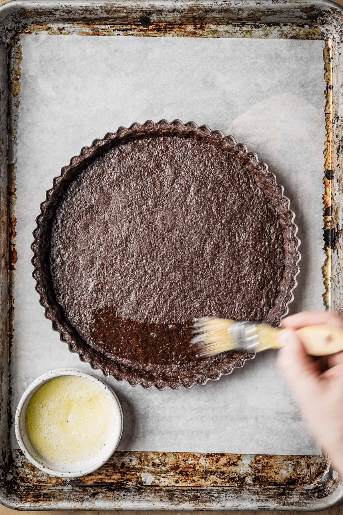 Egg wash being brushed onto a baked tart.