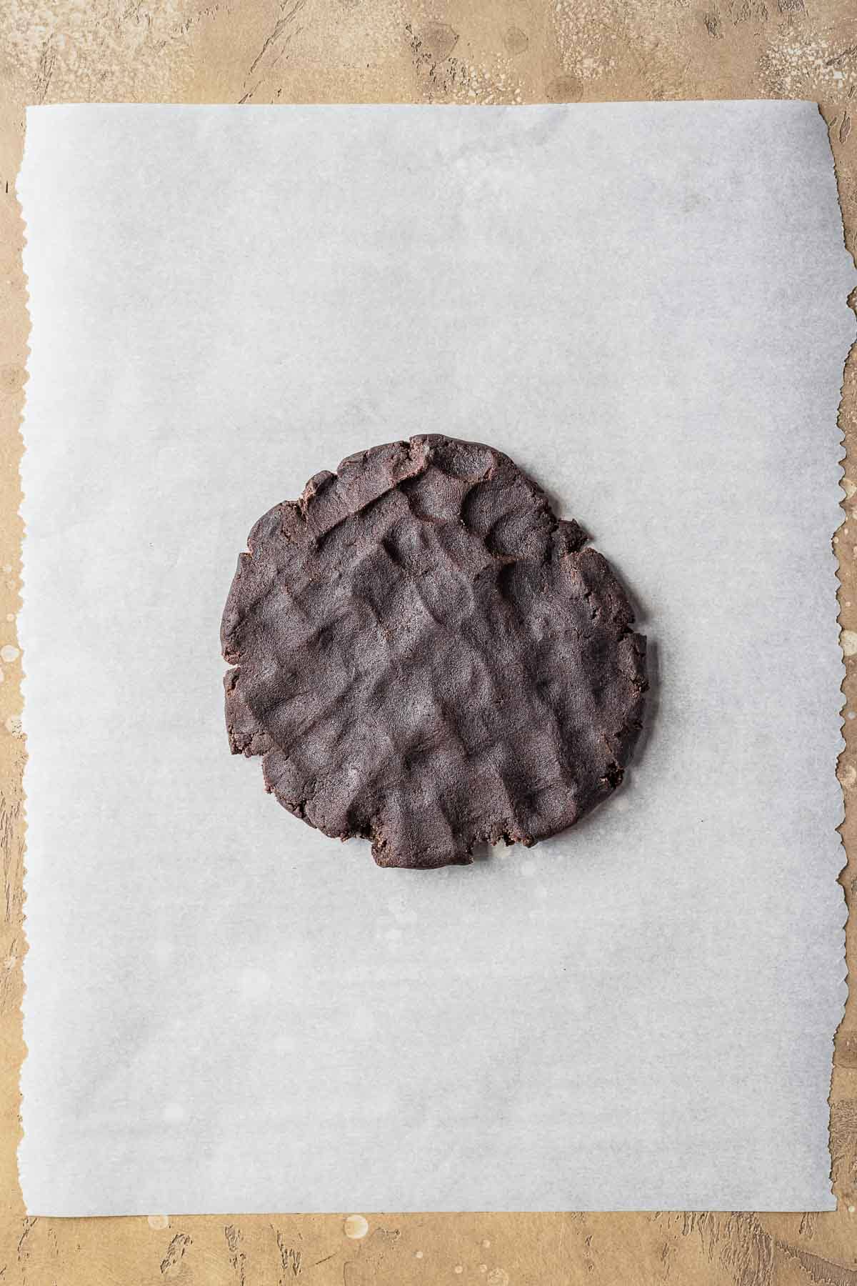 A disc of chocolate dough on parchment paper.