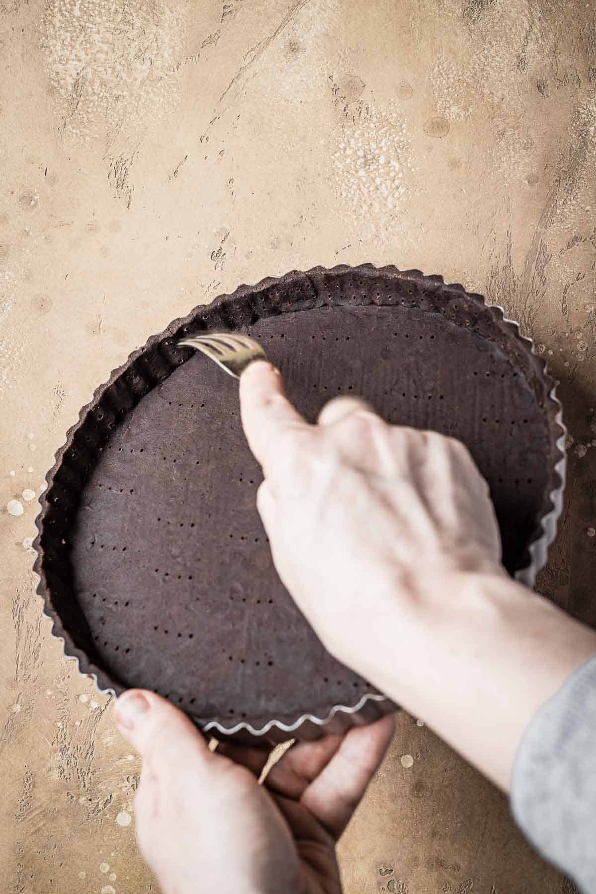 A hand docking the edges of an unbaked tart with a fork.