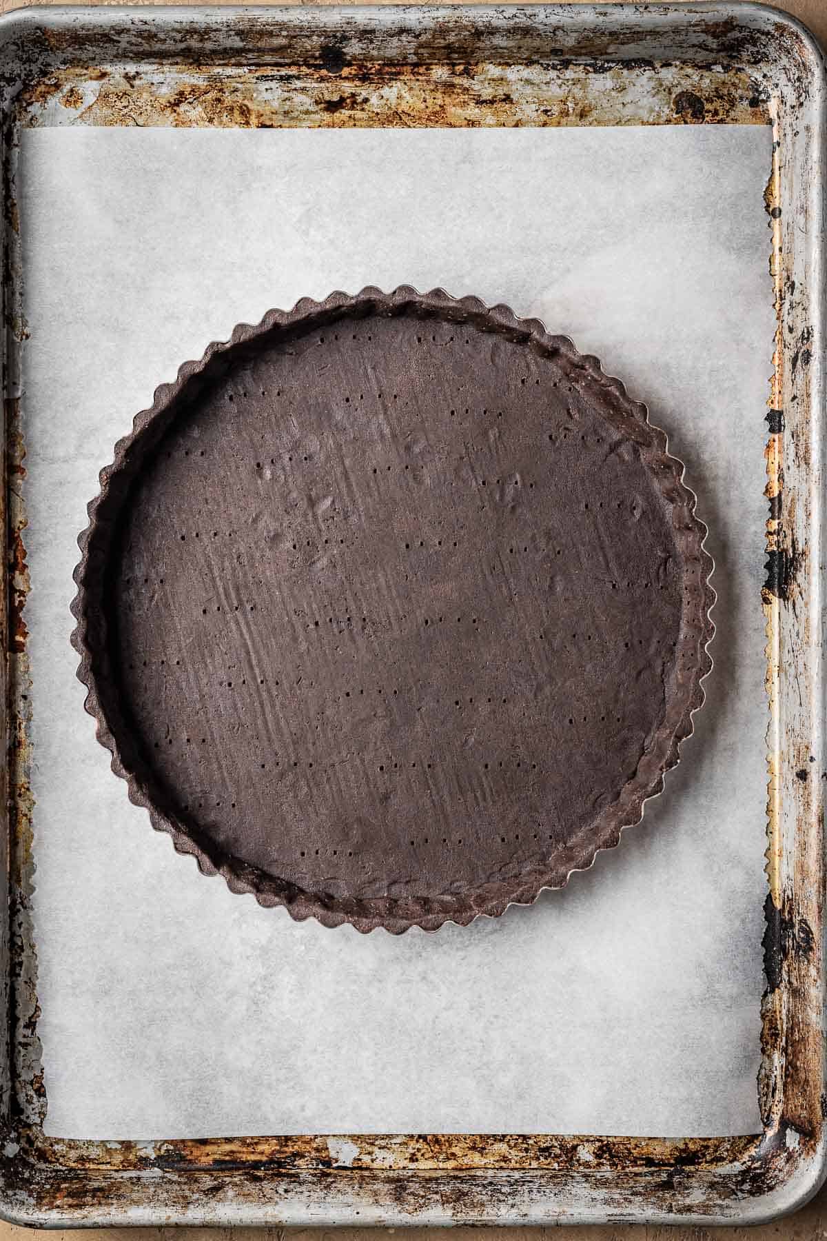An unbaked docked tart shell on a parchment lined baking sheet.