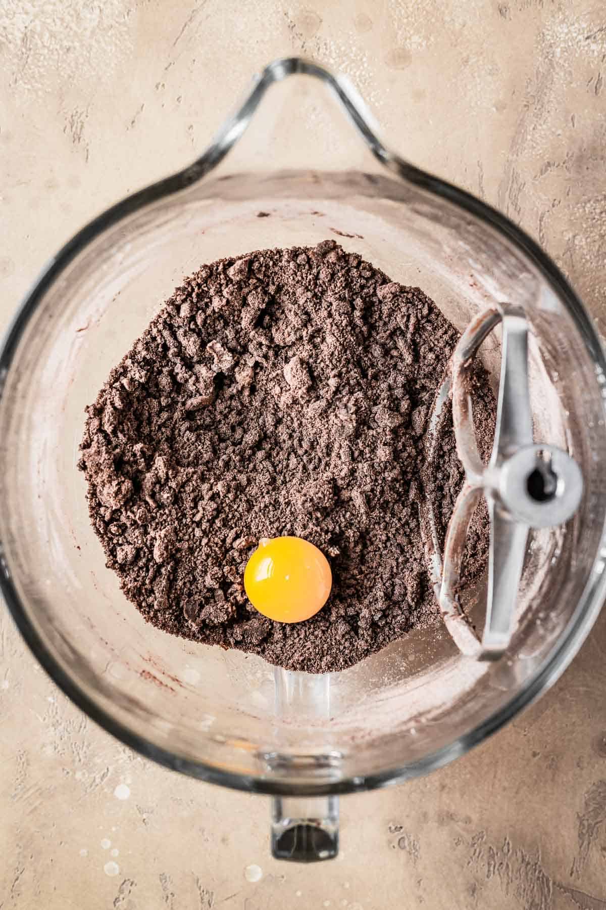 An egg yolk resting on dry ingredients and butter in a mixing bowl.