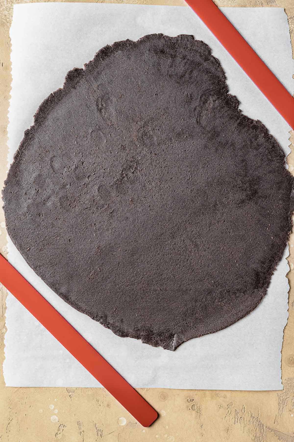 Chocolate tart dough rolled thinly on parchment paper.
