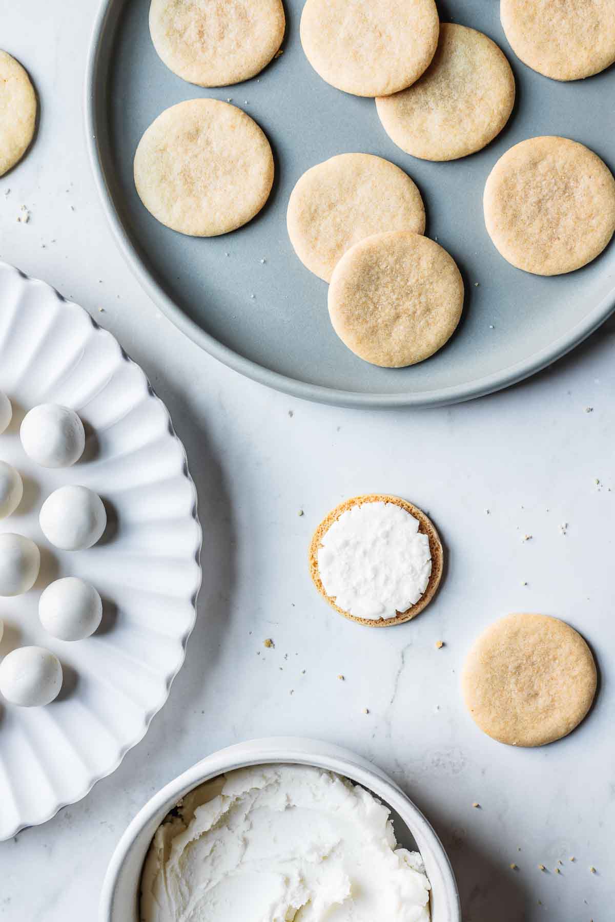 Round vanilla cookies and scoops of vanilla creme filling on plates ready to be sandwiched together.