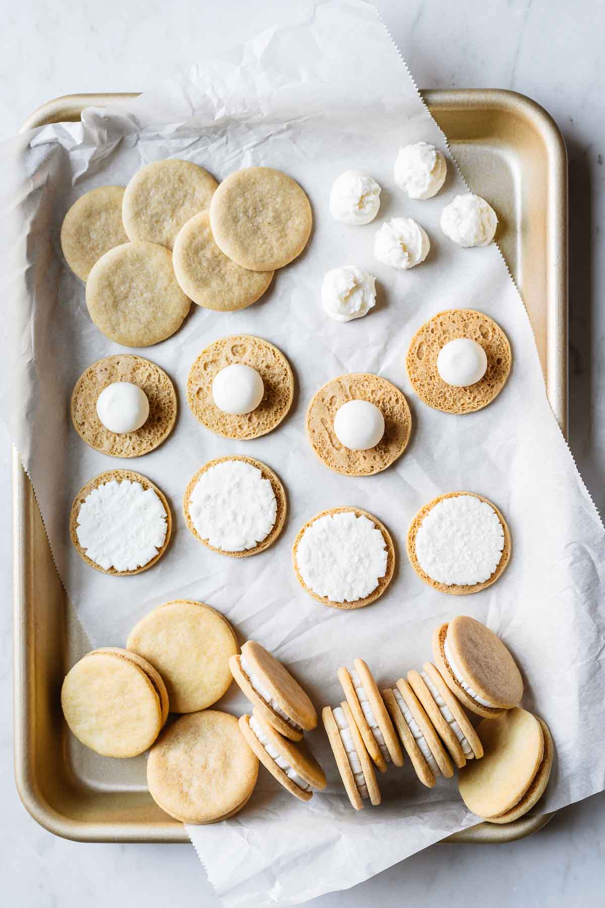 Homemade Golden Oreo cookies in different stages of assembly on a gold baking sheet.