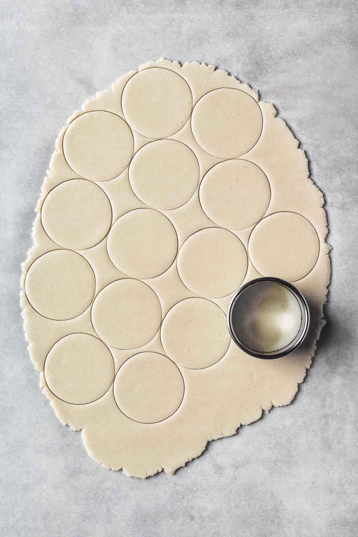 Thinly rolled vanilla cookie dough with circular cutouts.
