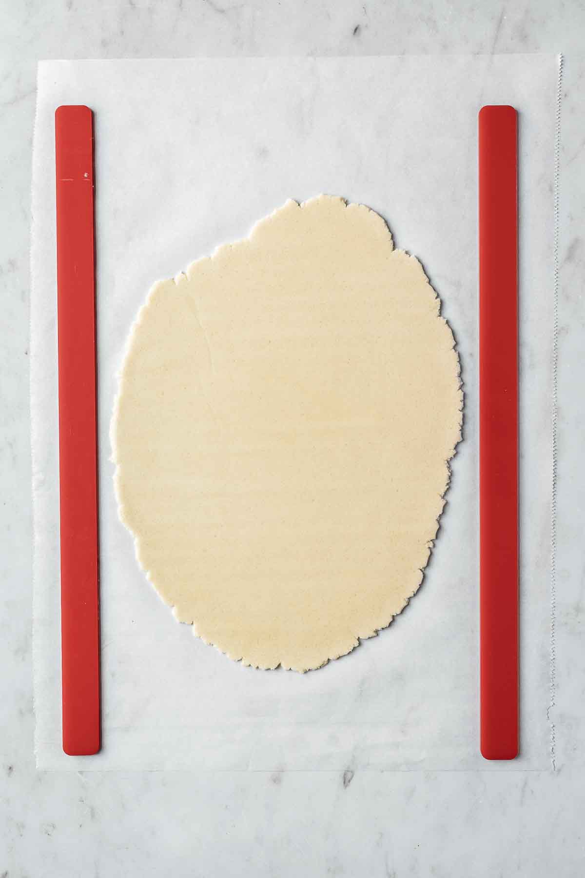Thinly rolled vanilla cookie dough on parchment paper with dough guides.