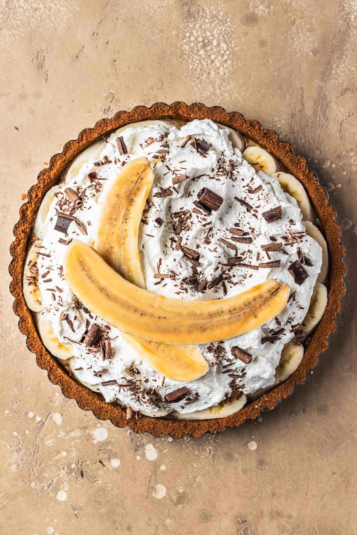 Banoffee tart with whipped cream, chocolate shavings and a banana sliced lengthways.