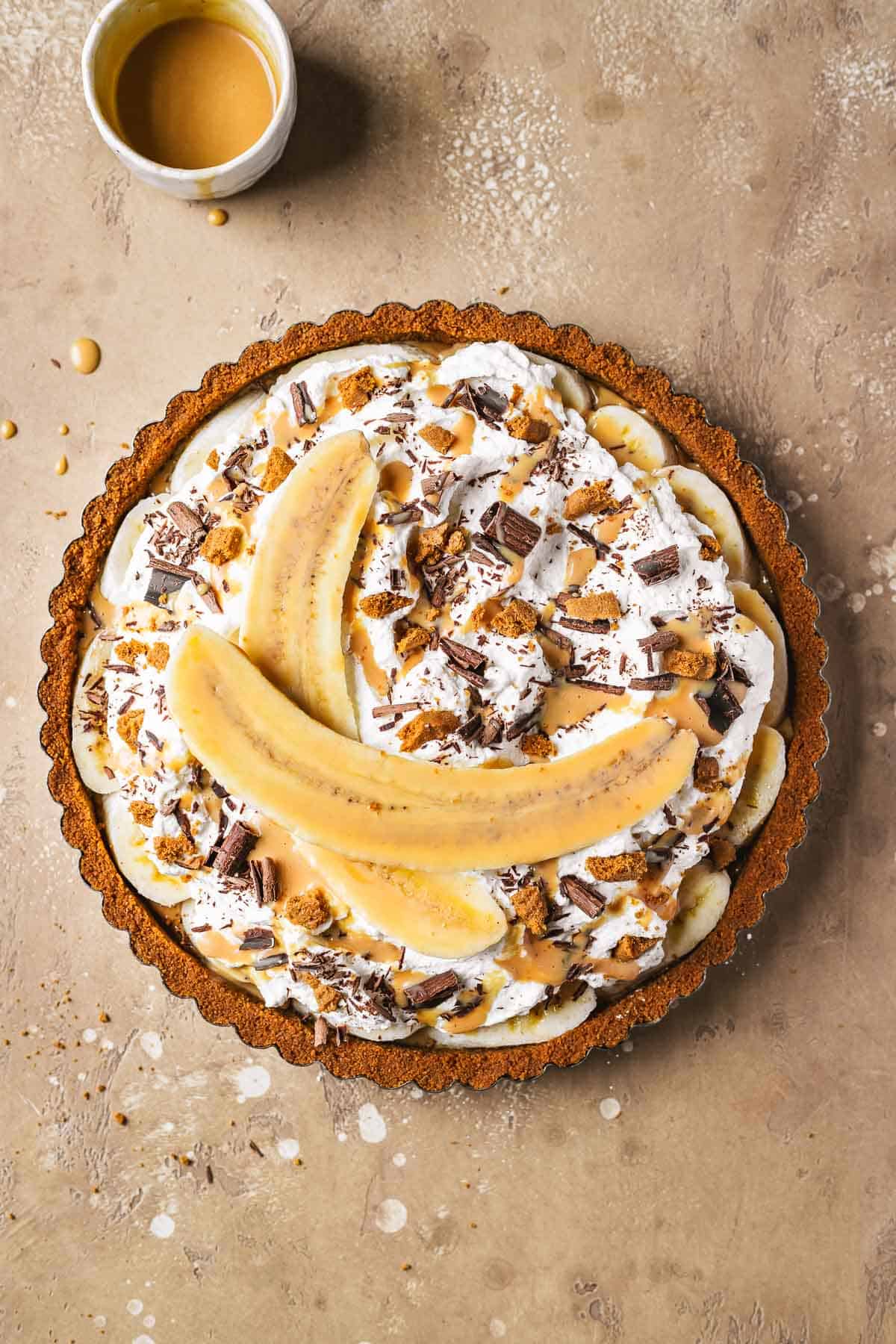 A banoffee tart topped with sliced banana, chocolate shavings, biscoff crumbles and dulce de leche sauce.