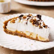 A slice of banoffee tart on a plate showing layers of dulce de leche, bananas and whipped cream.