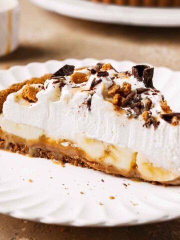 A slice of banoffee tart on a plate showing layers of dulce de leche, bananas and whipped cream.