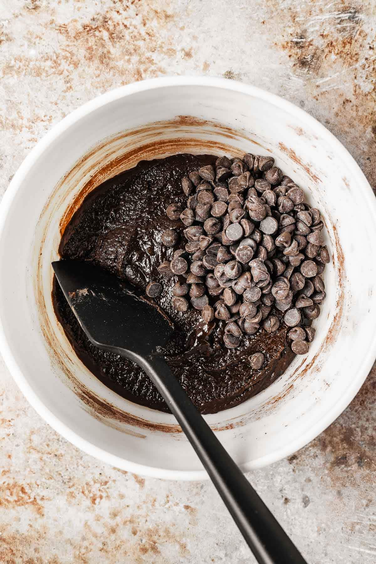 Chocolate chips being stirred into a mixing bowl of chocolate bar cookie batter.