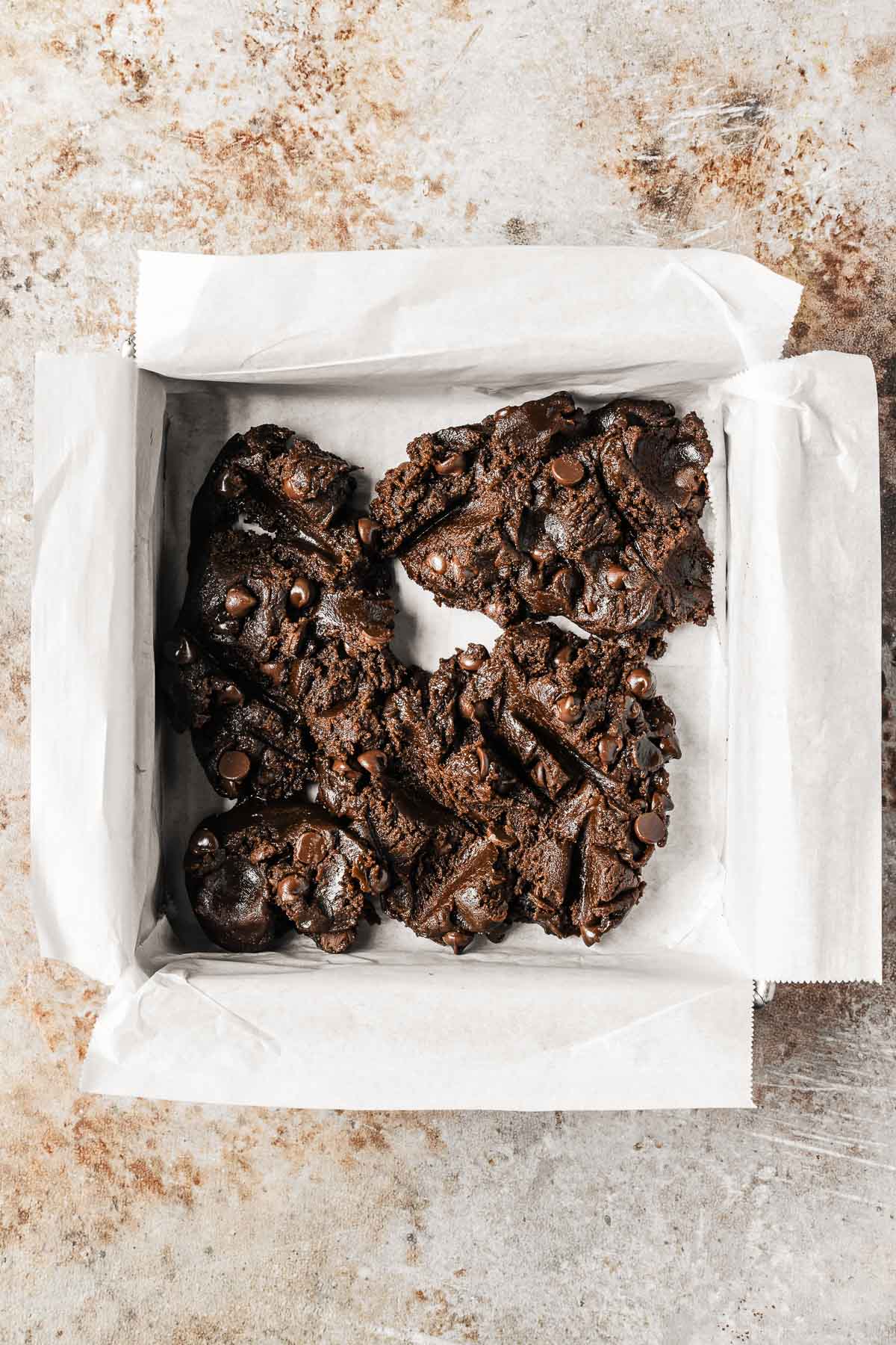 Dark chocolate dough being scooped into a parchment lined pan.
