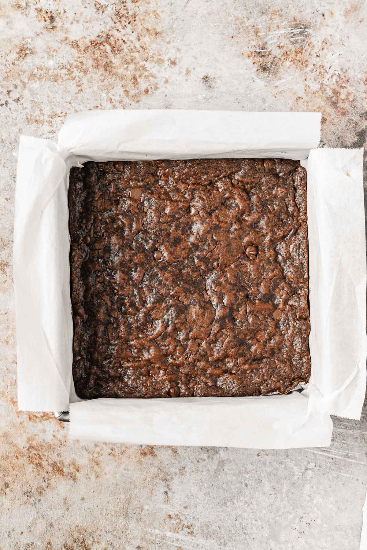 Baked chocolate chocolate chip cookie bars in a square parchment lined pan.