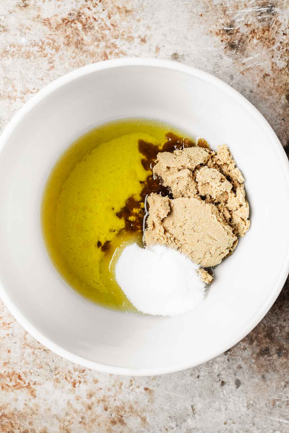 A white mixing bowl with oil and sugars.