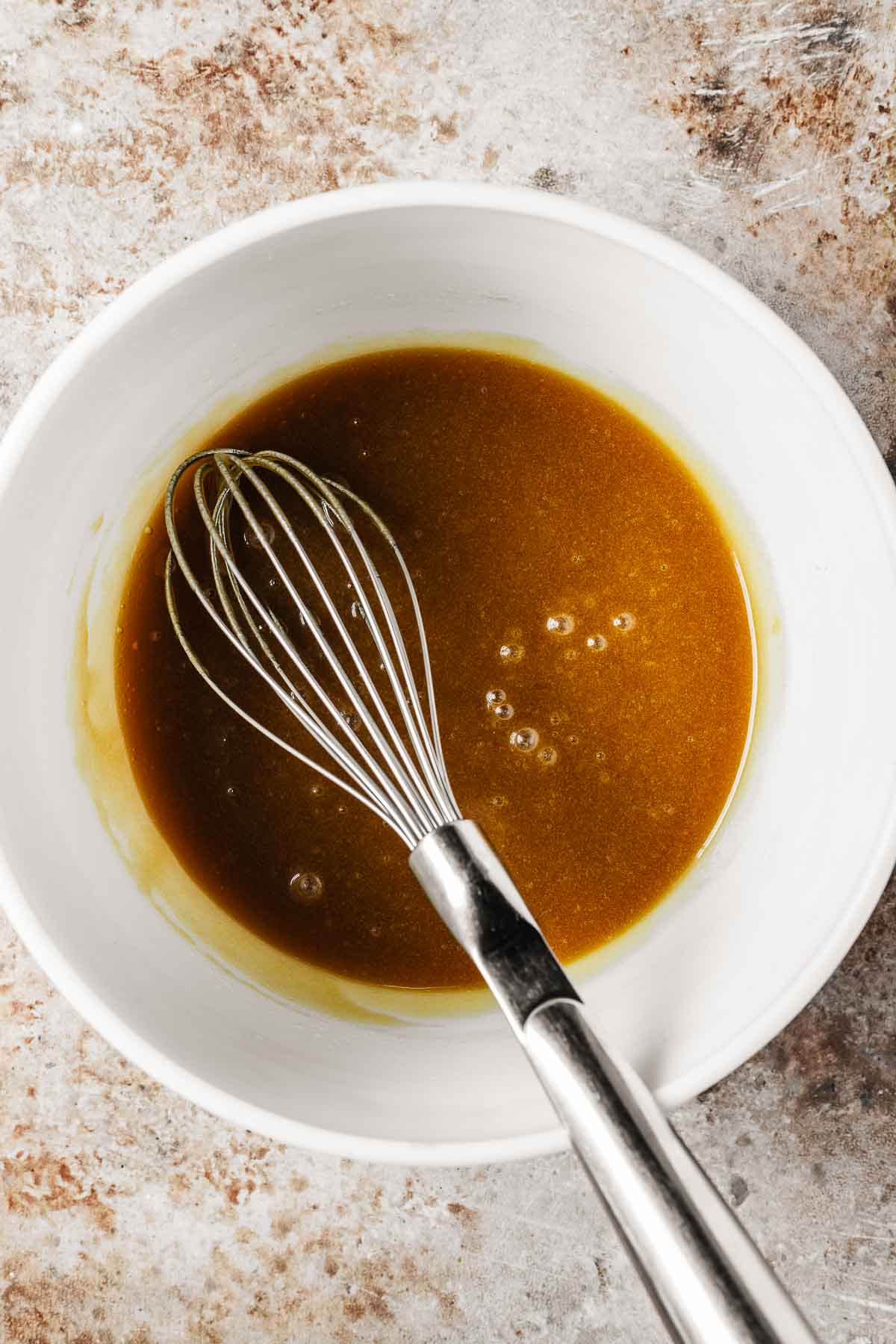 Liquid ingredients incorporated into fat and sugars in a mixing bowl.