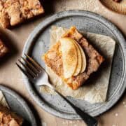 A slice of simple apple cake on a ceramic plate with three slices of fresh apple fanned out on top.
