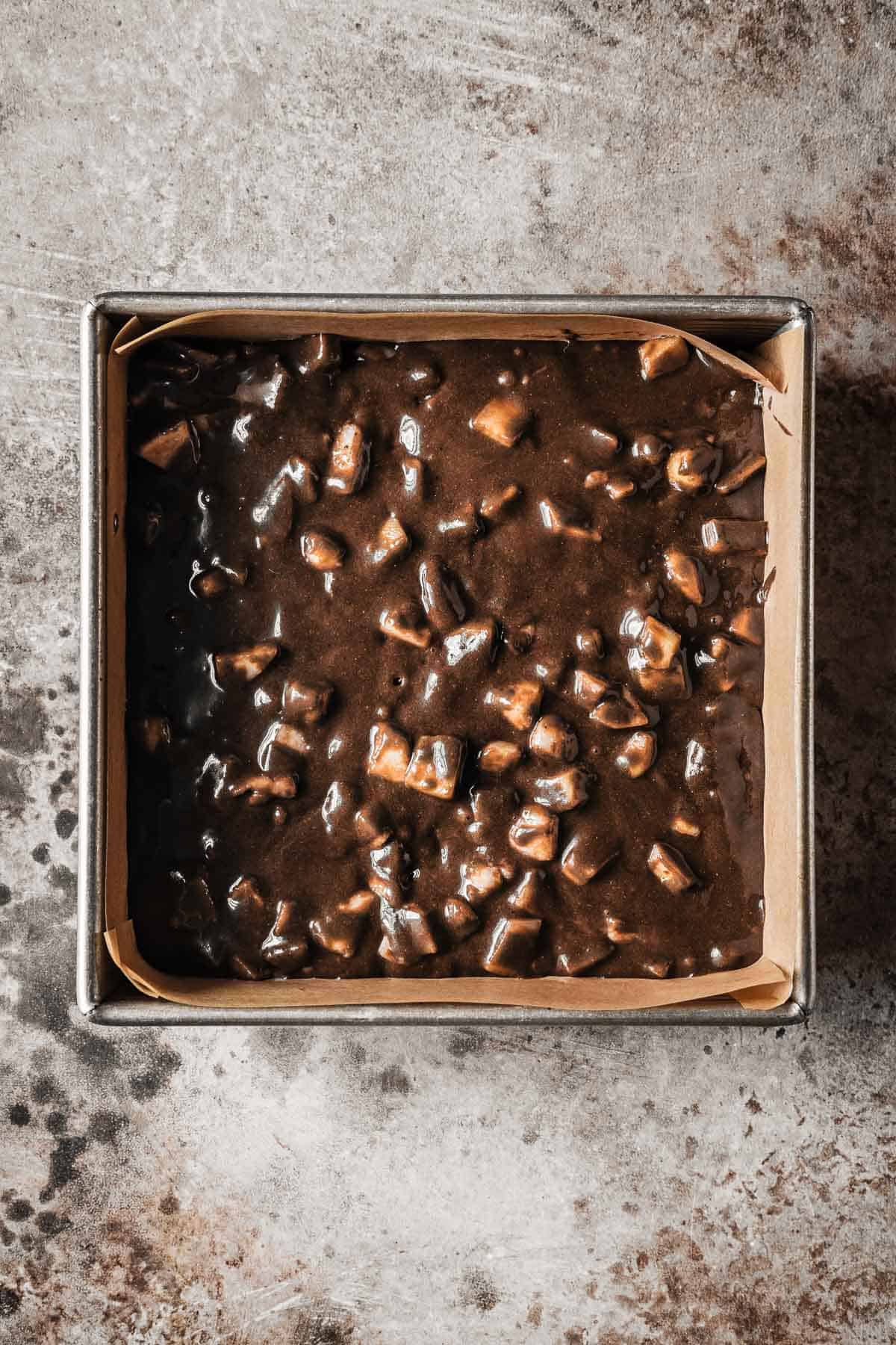 Chocolate pear cake batter in a parchment paper lined square pan.