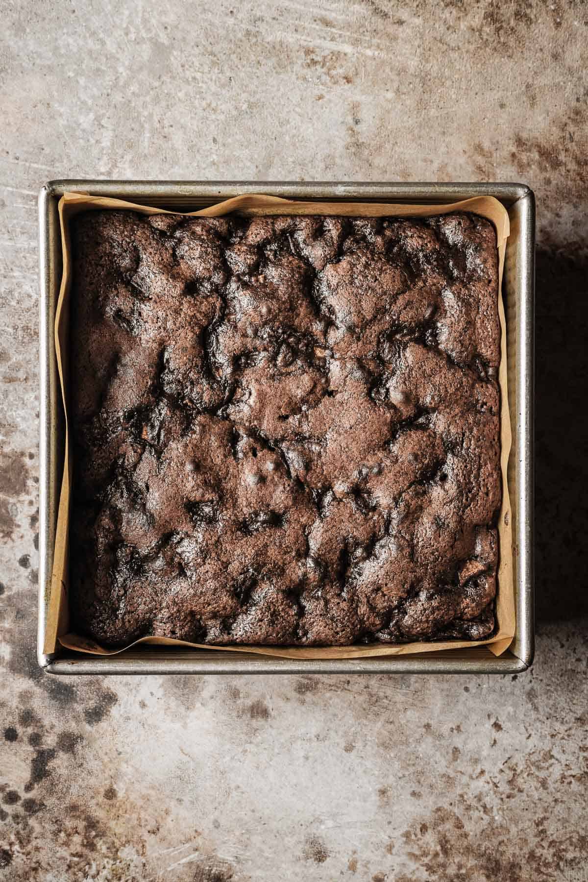 A baked chocolate pear cake in a square parchment lined metal pan.