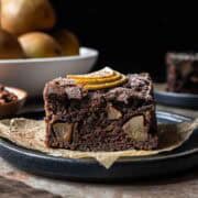 A square of chocolate pear cake from the side showing the crumb and fruit inside.