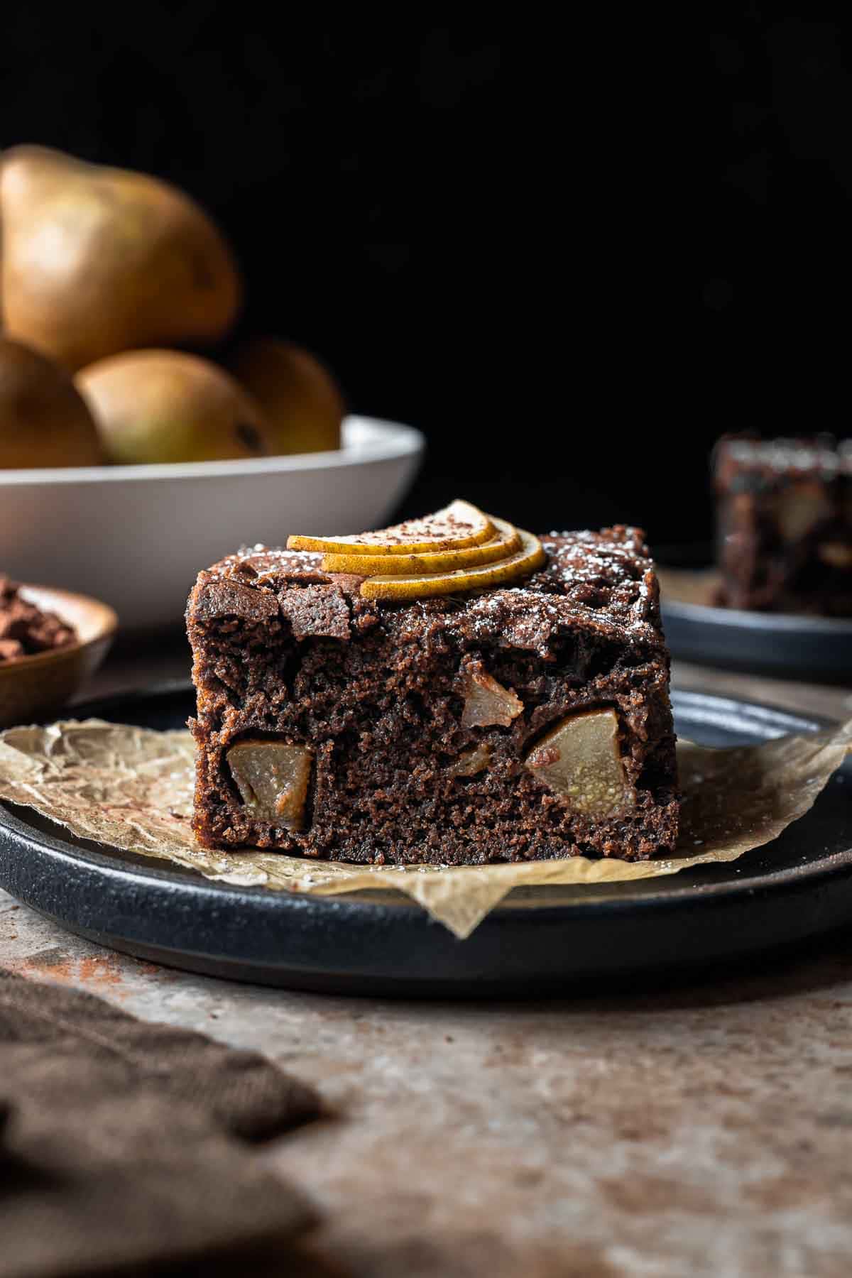 A square of chocolate pear cake from the side showing the crumb and fruit inside.