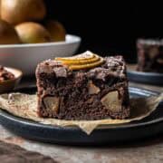 A square of chocolate pear cake from the side showing the crumb and fruit inside.
