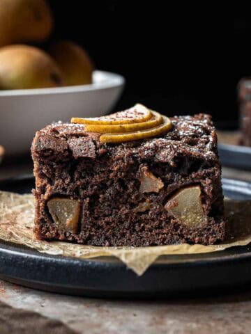 A square of chocolate pear cake from the side showing the crumb and fruit inside.