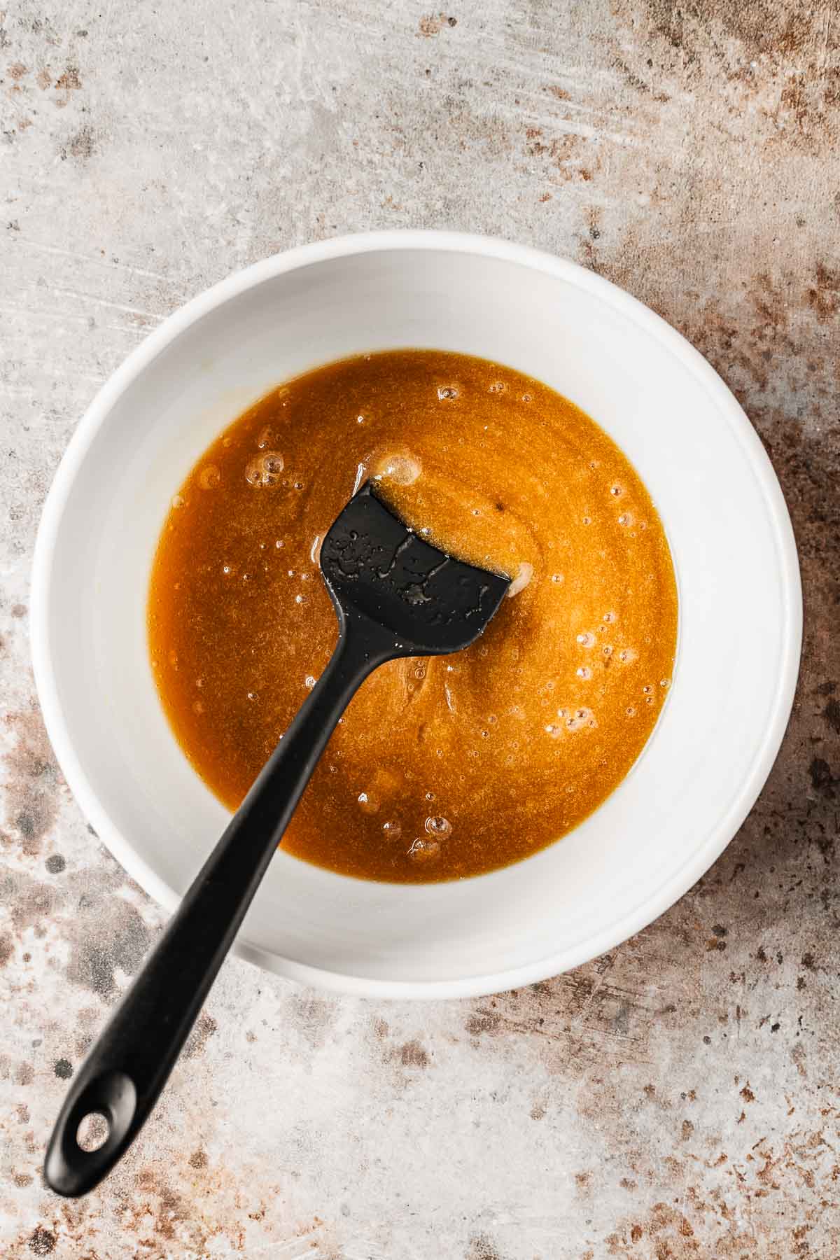 A mixing bowl with wet ingredients and a black spatula.
