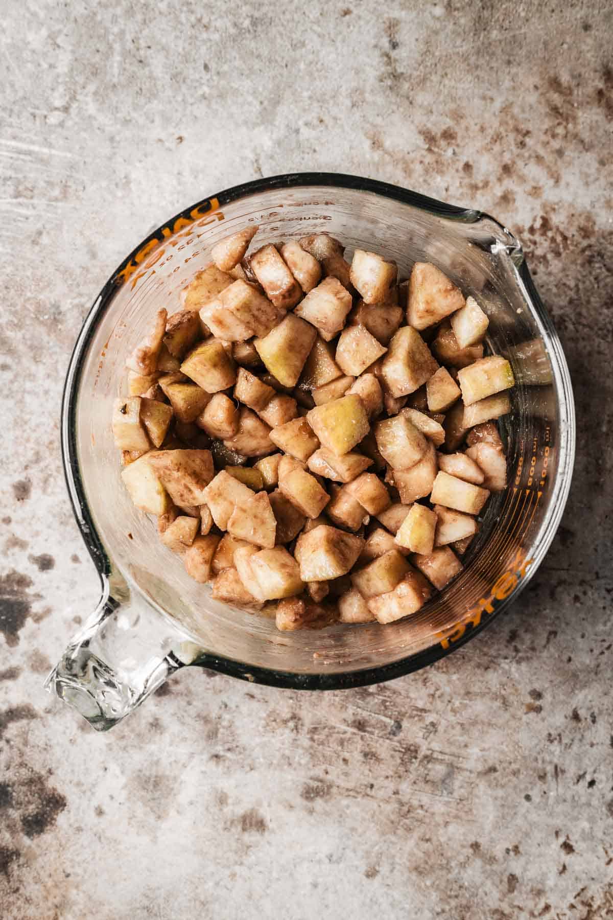 A glass measuring cup of diced pears coated in flour mixture.