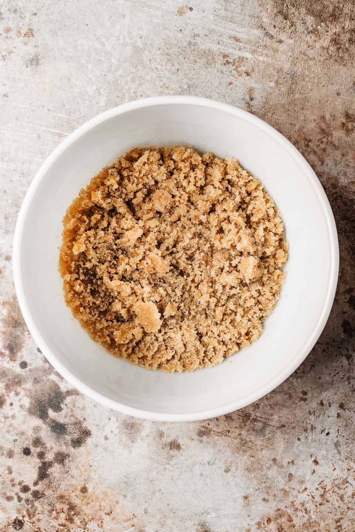 A mixing bowl with brown and white sugars mixed with oil.