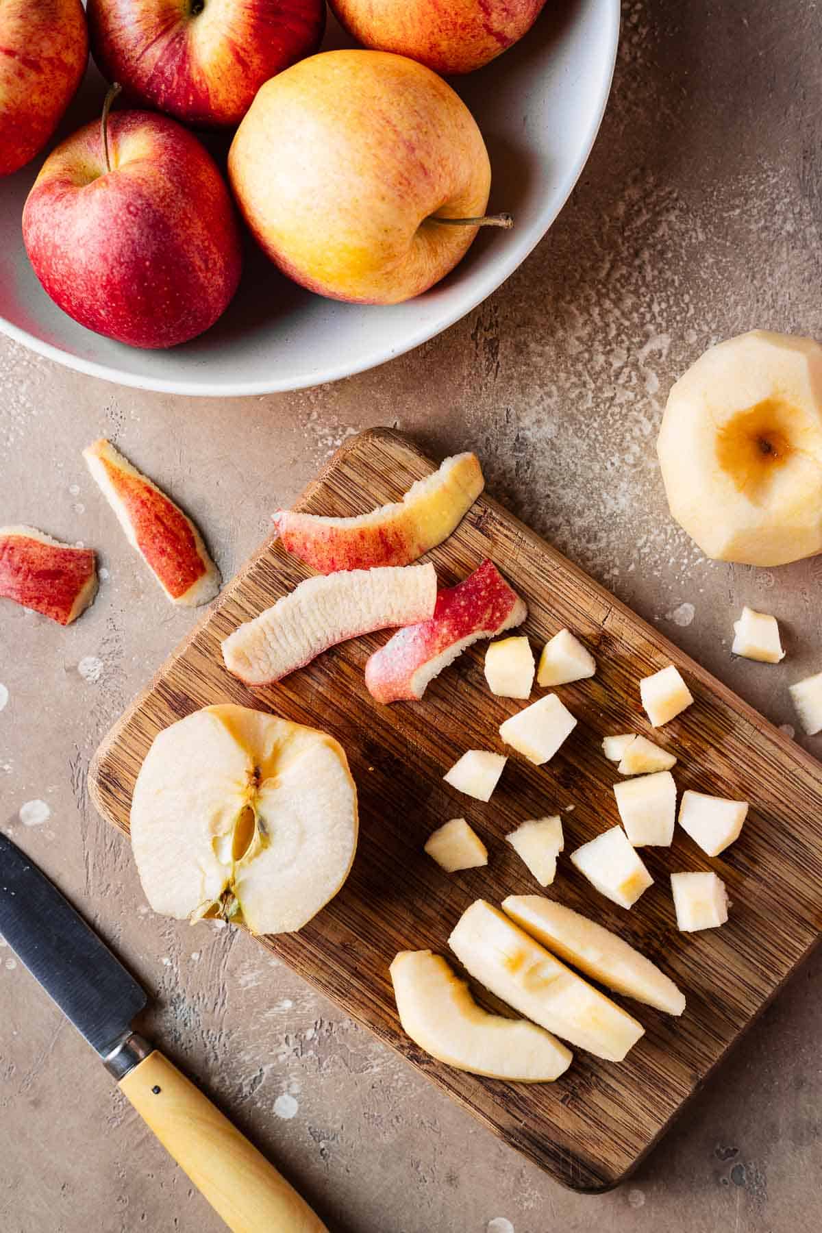 Fresh peeled, sliced and chopped apples on a cutting board with more apples in a bowl.