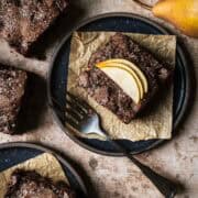A square of chocolate pear cake on a black ceramic plate.