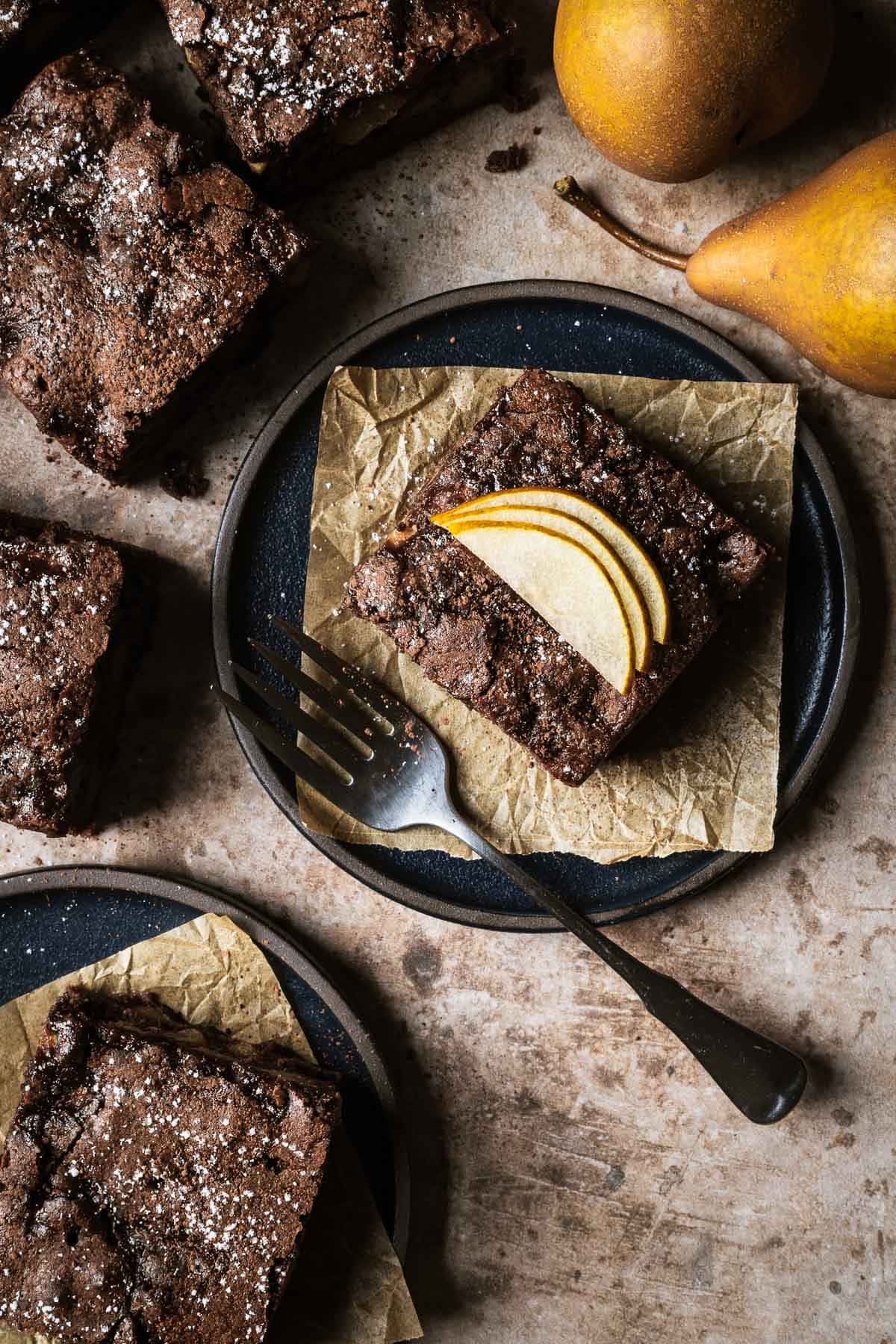 A square of chocolate pear cake on a black ceramic plate.