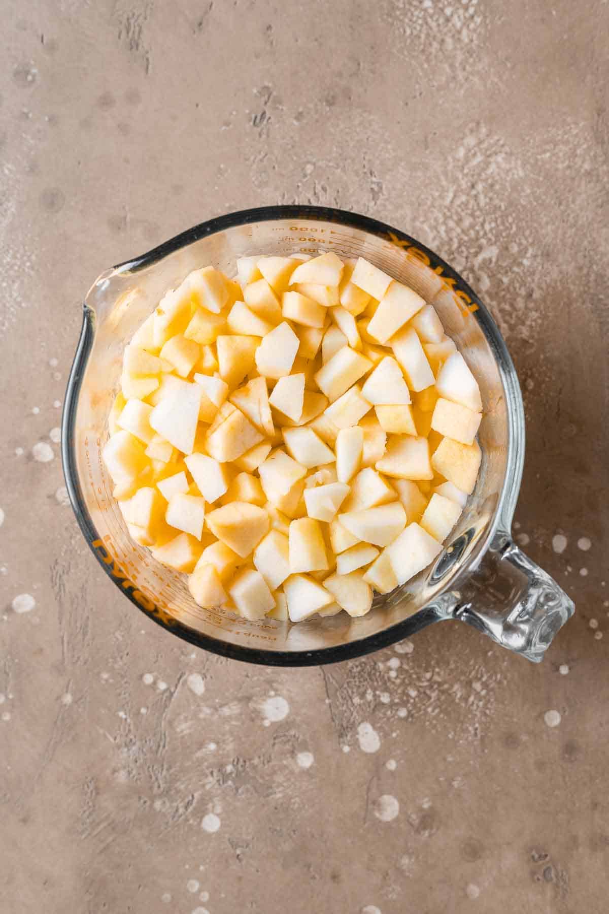 Chopped apples in a glass measuring bowl.