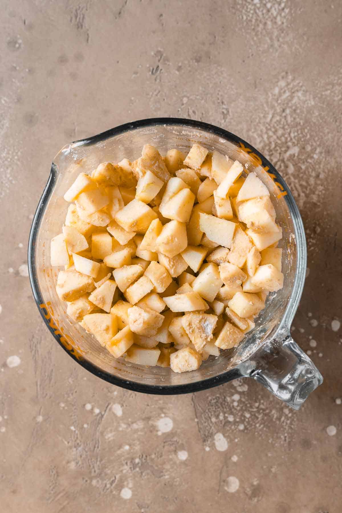 Chopped fresh apples tossed with flour in a glass measuring bowl.