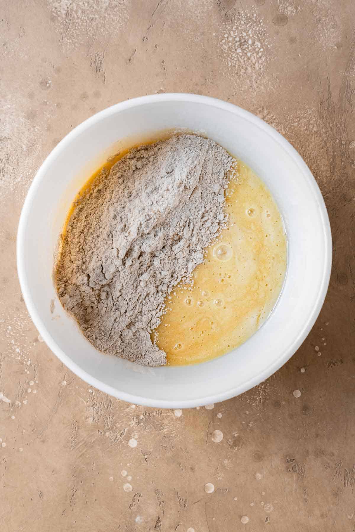 Wet and dry ingredients for simple apple cake in a white mixing bowl.