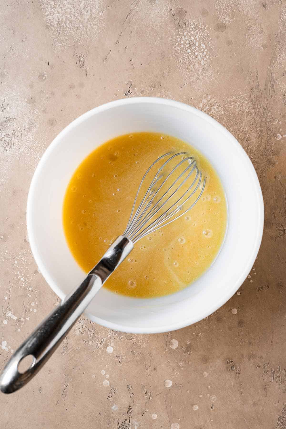 Eggs and vanilla whisked with sugar and oil in a mixing bowl.