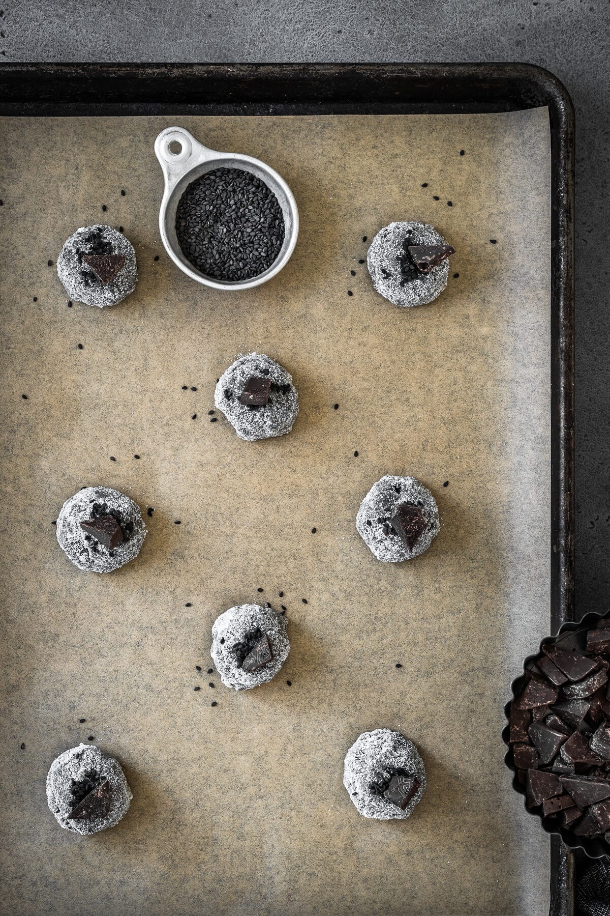 Balls of cookie dough rolled in sugar and topped with black sesame seeds and chocolate chunks.